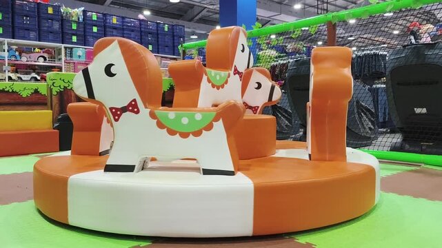 Colorful horse ride spinning in bright indoor playground for children to play and enjoy