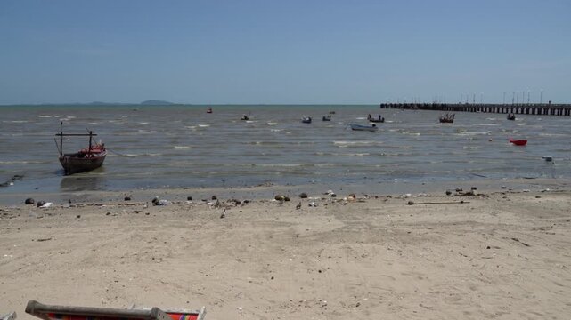 Fishing boats bobbing on the water near a long pier on a sunny day