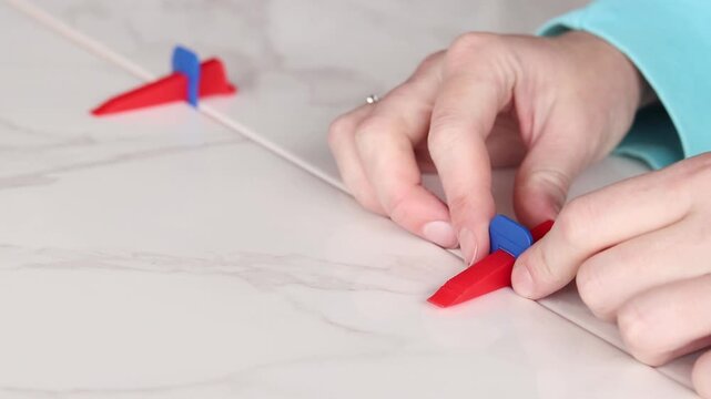 The master uses a plastic wedge and a base (clip) for perfect alignment of porcelain stoneware by level. Tile leveling system in the process of work. Modern auxiliary tools for professional tiling