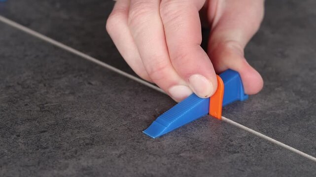 The master uses a plastic wedge and a base (clip) for perfect alignment of porcelain stoneware by level. Tile leveling system in the process of work. Modern auxiliary tools for professional tiling