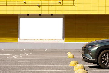 Large white billboard centered on yellow tiled storefront with closed metal shutters, parked car nearby, painted parking bays, bright daylight, clean urban retail exterior and empty forecourt © Маргарита Трушина