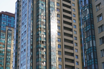 Fototapeta premium Glass facade skyscraper reflecting morning sunlight dense residential towers with geometric balconies and blue tinted windows, metal frames glinting, cityscape context suggesting sustainable
