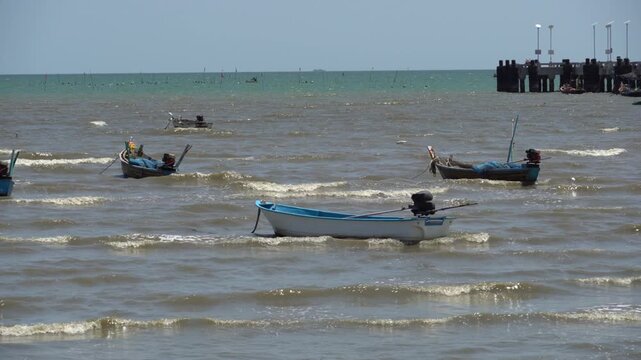 Small fishing boats bobbing on wavy ocean water near a pier