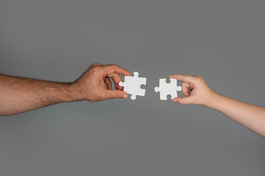 Puzzle create teamwork solution concept. Puzzle assembly shows planning and strategy. Human hands hold puzzle pieces together. Gray background makes puzzle symbol simple.