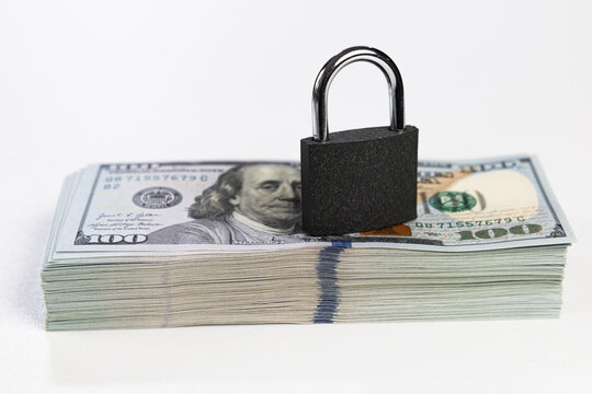 Closed black padlock on stack of US dollar banknotes isolated on white background