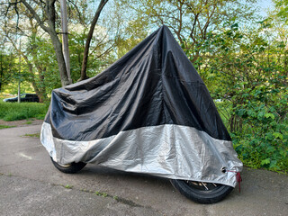 Black and gray fabric motorcycle cover protecting a parked bike in a residential yard surrounded by apartment buildings © Harmony Video Pro