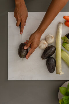 Overhead close up of hands cutting avocado on wooden cutting board
