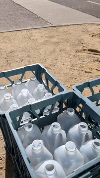 Crates hold many empty plastic bottles placed on sandy ground near a sidewalk