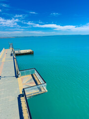 Fototapeta premium View of a long pier extending over calm blue waters under a clear sky with a few clouds during daytime at a coastal location