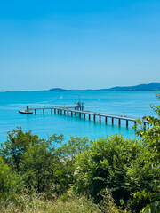 Fototapeta premium Dock extends into blue water with mountains in the distance on a clear sunny day at the seaside