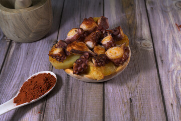 Fototapeta premium Traditional Spanish pulpo a la gallega or octopus with potatoes, paprika and olive oil served on a wooden plate over rustic grey background
