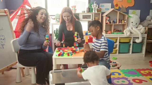 Women and children stacking colorful blocks with hands building a tall tower on a table in a preschool building; learning joy.