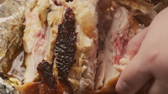 A woman's hands, using a sharp knife, cut a whole turkey baked with a spiced crust on foil. Medium shot.