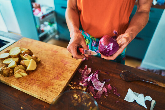 Woman preparing dinner - peeling onion with potatoes on the board