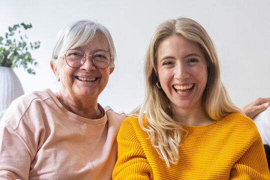 Grandmother and granddaughter sitting together on a sofa, smiling and laughing in a bright home, sharing a warm, affectionate moment of family, joy and intergenerational bonding