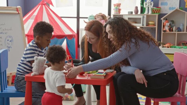Women teachers guide children drawing and passing a toy with hand extended at a red play table in a preschool classroom building; nurturing early learning.