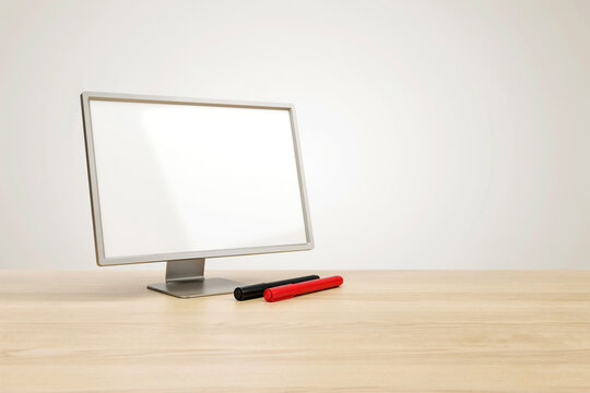 Flat-screen monitor on wooden desk with red markers desi