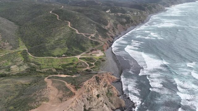 Aerial push in drone shot showing the rugged coastline and cliffs of the Fisherman's Trail, Rota Vicentina, near Aljezur, Portugal, with powerful ocean waves.