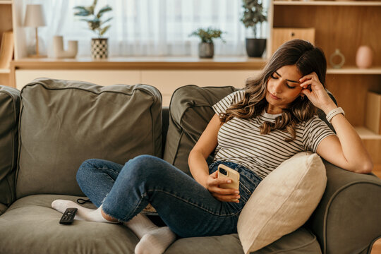 Young woman feeling bored on couch with smartphone
