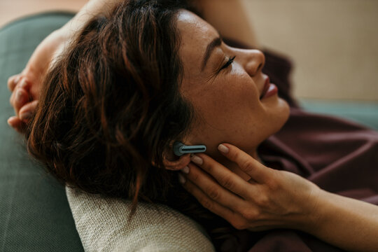 Woman relaxing at home listening to music on earbuds