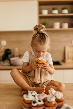 Little girl sitting on kitchen counter eating cupcake
