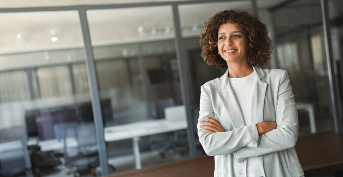 Smiling young multiracial businesswoman standing in professional office. Happy latin or indian woman confident smile looking aside at copy space. Web banner corporate portrait business for website, ad