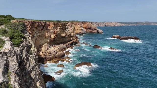 Aerial drone shot featuring a push in movement over the rugged cliffs and turquoise waters of the Sagres coastline in Portugal, part of the Fisherman's Trail on the Rota Vicentina.