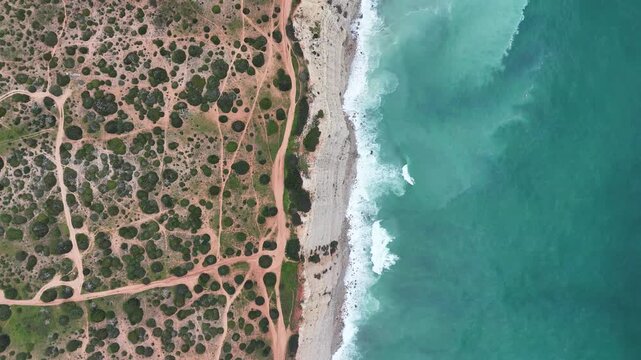 Aerial drone top down shot pushing in on the rugged coastline of the Fisherman's Trail, part of the Rota Vicentina in Portugal. Waves crash on sandy and rocky shores.