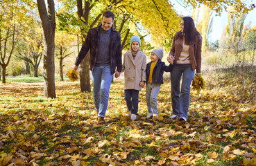 Naklejka premium Family with parents and children walking in autumn. Smiling mother and father hold hands with boy and girl in a park with leaves, enjoying outdoor time. Clear concept of family unity and care.
