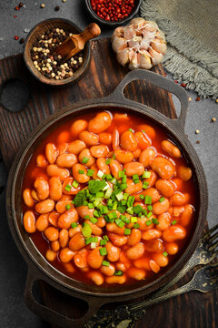 Boiled beans with tomato sauce and tomatoes. With basil and parsley. On a gray stone background. Close-up. Healthy food.