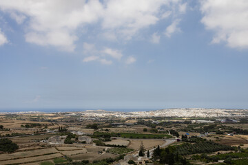 Fototapeta premium Panoramic view of Maltese countryside and distant towns under a cloudy blue sky.