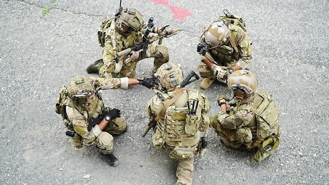 Special forces team in training on a gray surface discussing tactics at a remote location in the afternoon