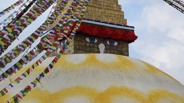 Close-up of the iconic Boudhanath Stupa in Kathmandu, Nepal, featuring the famous Buddha eyes painted on the white dome. Colorful Tibetan Buddhist prayer flags flutter in the wind