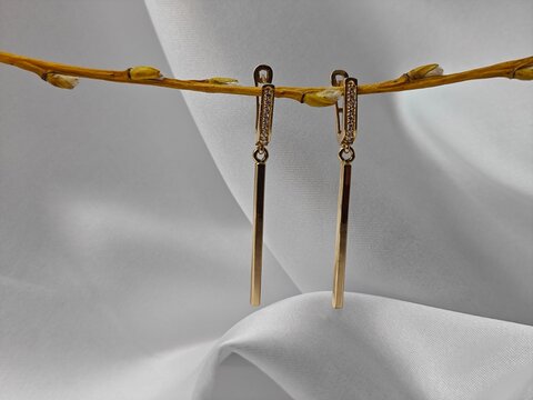 Gold dangle earrings hanging from a horizontal twig. Minimalist bar jewelry displayed on white fabric background