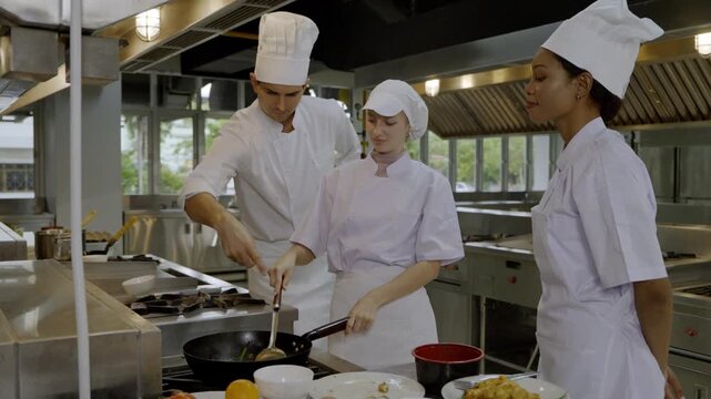Cooks learn techniques in a busy kitchen during a culinary class with chefs and students working together