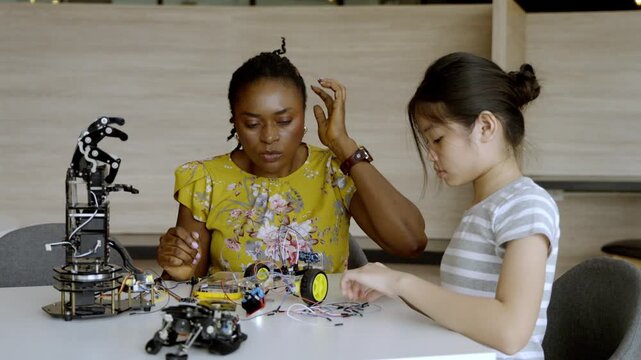 Woman teaches girl about robotics in a workshop setting with various tools and materials