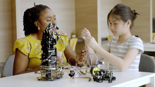 Young girl and adult build robot using wires and parts in a classroom setting during a workshop in the afternoon