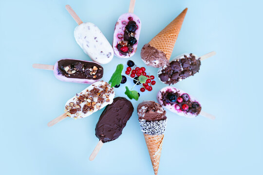 Colorful round of homemade yogurt and milk ice pops. Vanilla and chocolate decorated with nuts and frozen berries on bright blue background. Perfect for a summer children's birthday party. Top view.