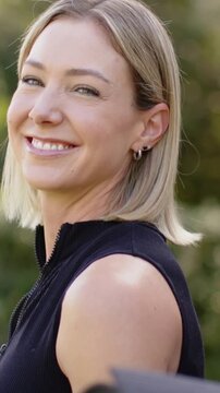Vertical video: Smiling woman turning and laughing at park, hand touching shoulder in black zip-top