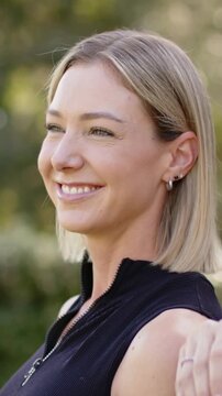 Vertical video: Smiling woman in black tank laughing after friend placing arm on shoulder in park