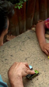 Vertical video: Leaning in, man in teal shirt pushing green car on concrete ledge for shared play