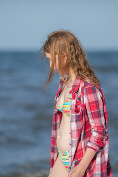 Girl in red plaid shirt standing by sea waves on beach.