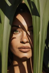 Beautiful young woman face peeking through green tropical leaves with sun shadows © eugenepartyzan
