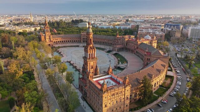 Central fountain flows in Plaza de Espana, Seville, Spain. Historic brick towers surround square in Seville, Spain in this aerial UHD. Water canal borders semicircular architecture in Seville, Spain