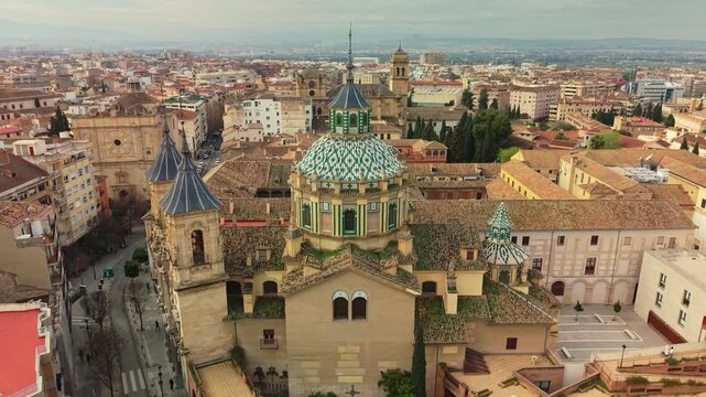 Dense Andalusian cityscape surrounds historic Basilica de San Juan de Dios in Granada, Spain. Aerial 4K explores ornate green tiled dome and ancient stone towers in beautiful Granada