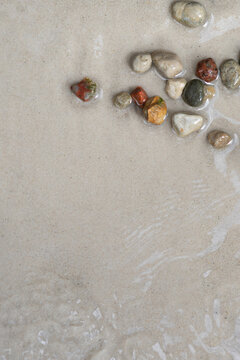 Colorful pebbles on sandy beach with shallow water, natural summer background with copy space
