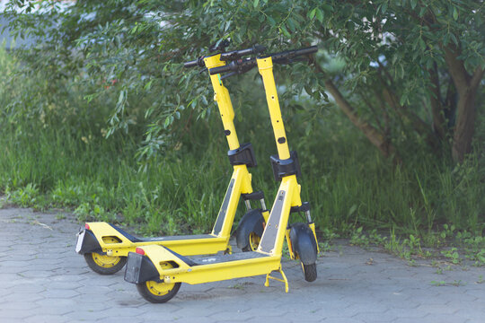 Two yellow electric scooters parked on a paved path outdoors, urban mobility, shared transport, eco travel, modern city lifestyle.