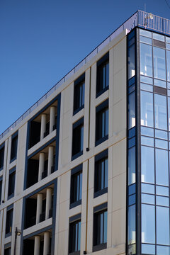 Tall modern apartment building with glass balconies against blue sky, urban architecture, residential real estate, contemporary facade design.