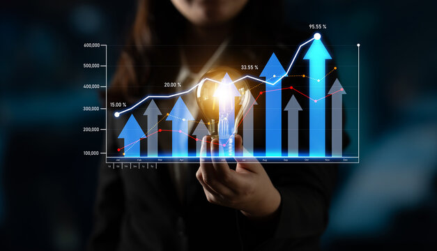 A businesswoman holds a light bulb while showcasing a financial growth graph with ascending arrows, symbolizing innovation and success in a modern workspace. Scalp