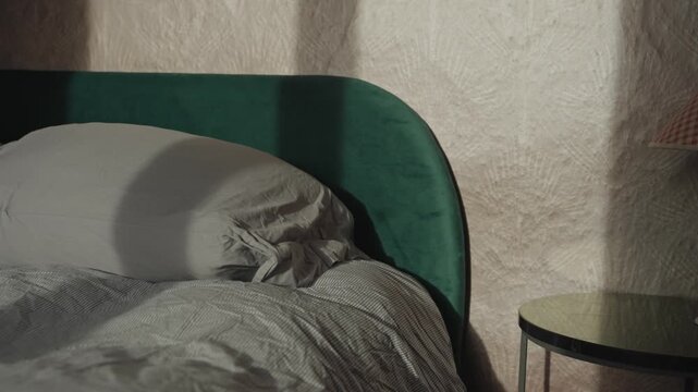 Early morning sunlight and shadows illuminating bedroom and rumpled sheets and pillows of unmade bed. Calm and tranquility in small house in countryside or family town hotel in village. Cozy and warm